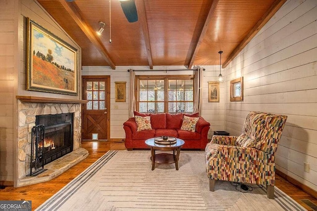 living room with wood ceiling, wood-type flooring, vaulted ceiling with beams, a stone fireplace, and wood walls