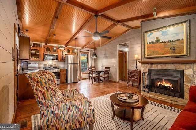 living room featuring wood walls, a stone fireplace, sink, vaulted ceiling with beams, and light wood-type flooring