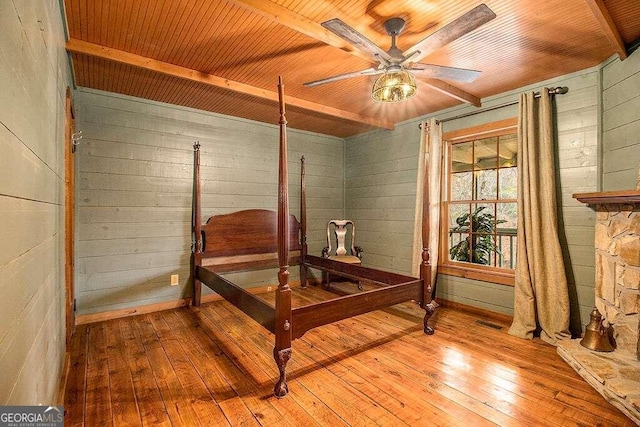 bedroom featuring light wood-type flooring, ceiling fan, wooden walls, wooden ceiling, and beamed ceiling