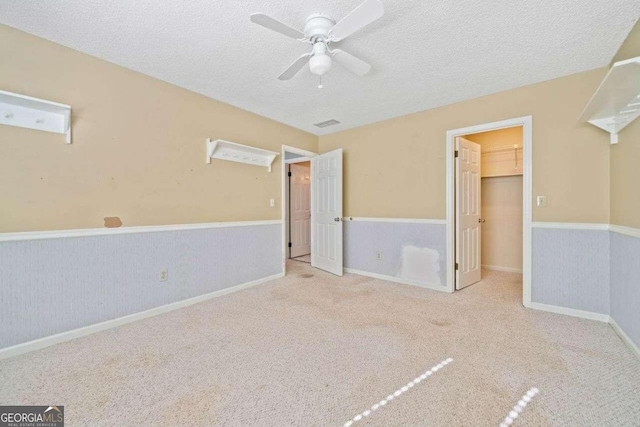 unfurnished bedroom featuring ceiling fan, a spacious closet, a textured ceiling, light colored carpet, and a closet