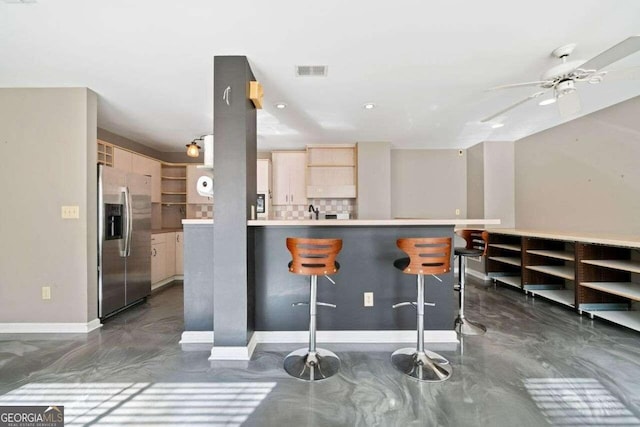 kitchen featuring a kitchen bar, stainless steel refrigerator with ice dispenser, decorative backsplash, kitchen peninsula, and light brown cabinets