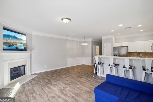 living room featuring light wood-type flooring, crown molding, and a chandelier