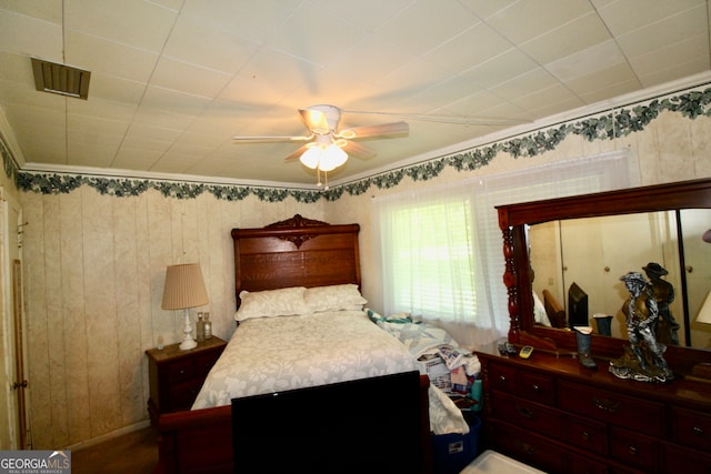 bedroom with ceiling fan, ornamental molding, and wood walls