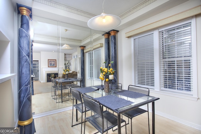 dining room with a fireplace, crown molding, decorative columns, light wood-type flooring, and baseboards