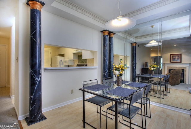 dining area with a fireplace, wood finished floors, baseboards, ornamental molding, and decorative columns