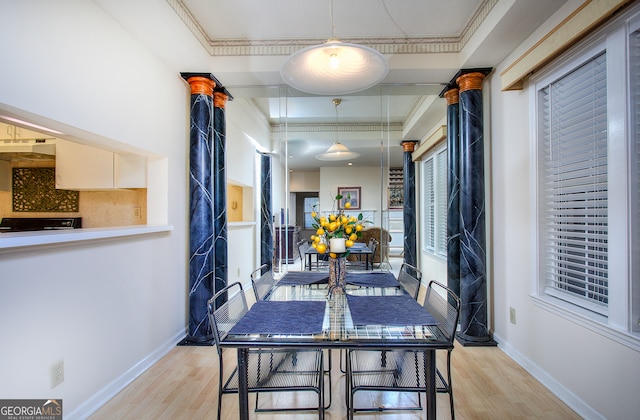 dining area featuring light hardwood / wood-style floors, a tray ceiling, crown molding, and decorative columns