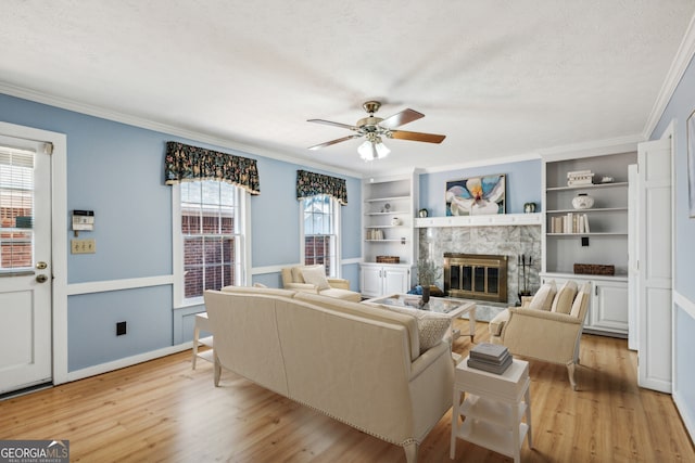 living room featuring ceiling fan, crown molding, a textured ceiling, a fireplace, and light wood-type flooring