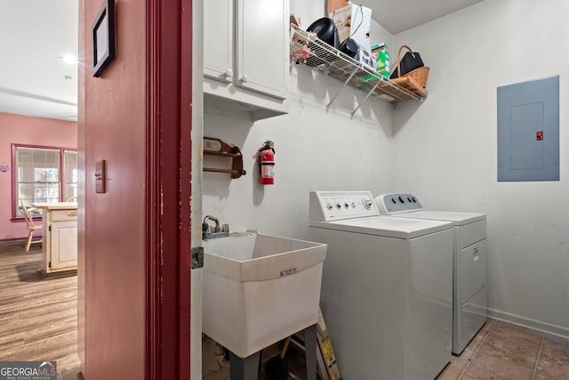 laundry area featuring washing machine and clothes dryer, sink, cabinets, electric panel, and light wood-type flooring