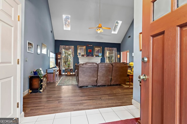 living room with ceiling fan, light wood-type flooring, high vaulted ceiling, and a skylight