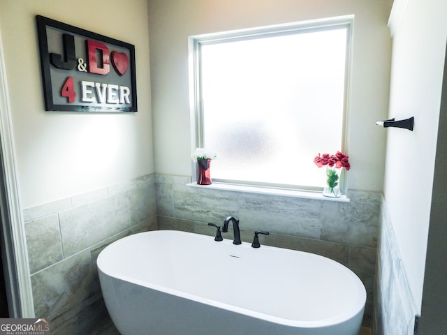 bathroom featuring a wealth of natural light, a washtub, and tile walls