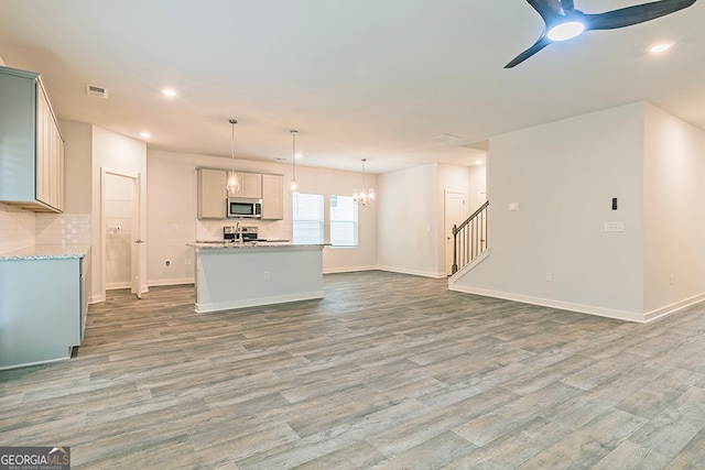 kitchen with pendant lighting, ceiling fan with notable chandelier, stainless steel appliances, and hardwood / wood-style floors