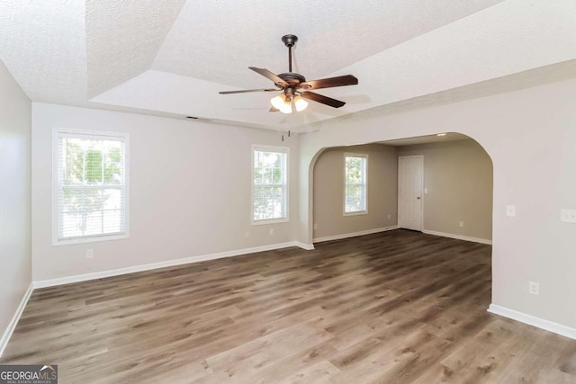 empty room featuring a textured ceiling, hardwood / wood-style flooring, plenty of natural light, and ceiling fan