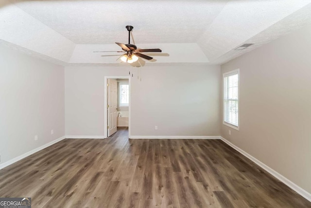 empty room with a tray ceiling, ceiling fan, a textured ceiling, and dark hardwood / wood-style floors