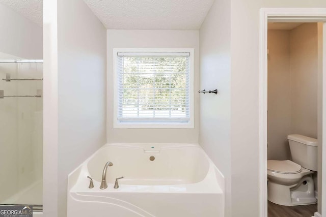 bathroom featuring a bathing tub, wood-type flooring, a textured ceiling, and toilet