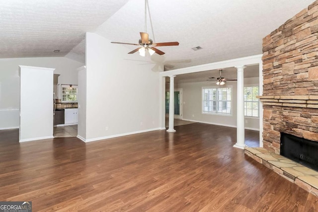 unfurnished living room featuring a textured ceiling, dark hardwood / wood-style flooring, vaulted ceiling, and a stone fireplace