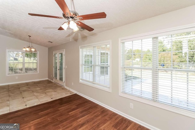 interior space featuring hardwood / wood-style floors, ceiling fan with notable chandelier, lofted ceiling, and a textured ceiling