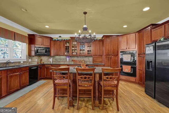 kitchen with black appliances, a breakfast bar, light wood-type flooring, and hanging light fixtures