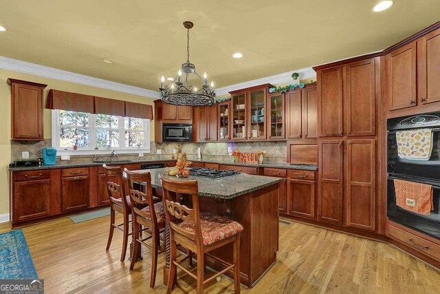 kitchen featuring a kitchen breakfast bar, crown molding, black appliances, light hardwood / wood-style flooring, and a kitchen island