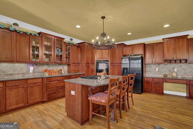 kitchen with pendant lighting, black appliances, light stone countertops, light wood-type flooring, and a kitchen island