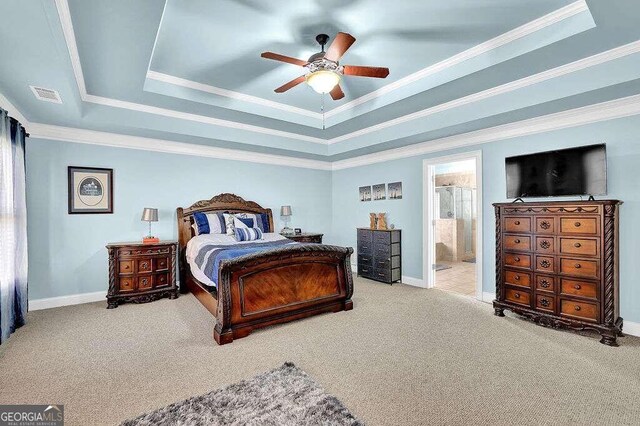 carpeted bedroom featuring a tray ceiling, ensuite bathroom, crown molding, and ceiling fan