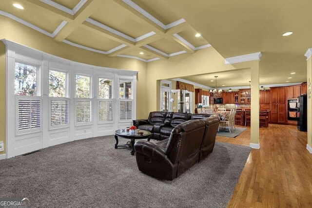 living room with a chandelier, beamed ceiling, light wood-type flooring, and crown molding