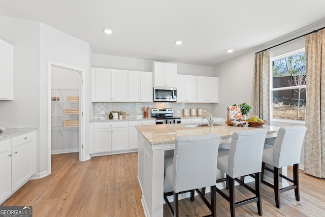 kitchen featuring white cabinets, sink, light wood-type flooring, an island with sink, and stainless steel appliances