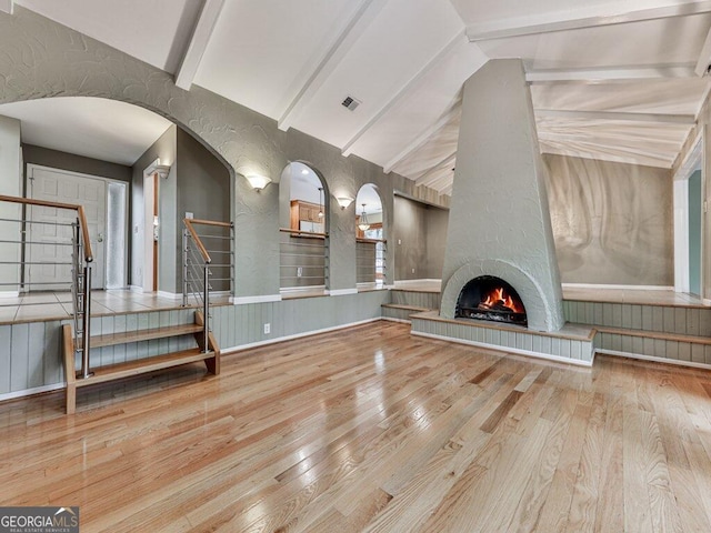 unfurnished living room with a fireplace, light wood-type flooring, and lofted ceiling with beams