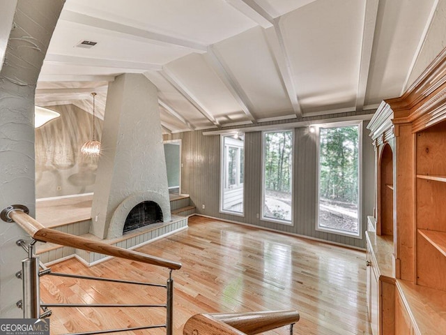 living room with a notable chandelier, lofted ceiling with beams, light hardwood / wood-style floors, and a tiled fireplace