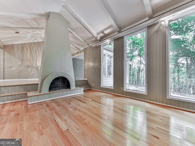 unfurnished living room with vaulted ceiling with beams, wood walls, a large fireplace, and wood-type flooring