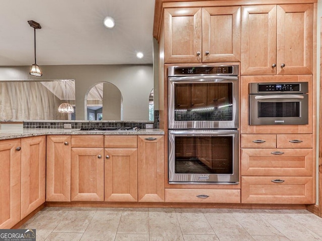 kitchen with appliances with stainless steel finishes, light stone counters, and pendant lighting