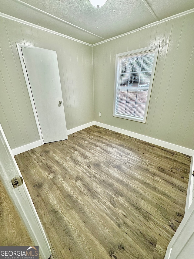 empty room with hardwood / wood-style floors, a textured ceiling, and wooden walls