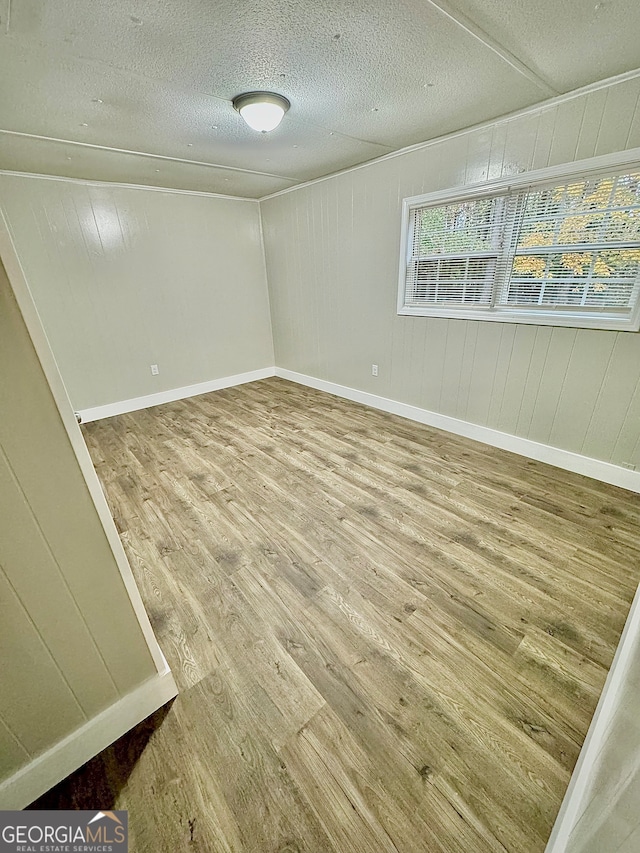 unfurnished room featuring wood walls, a textured ceiling, and hardwood / wood-style flooring