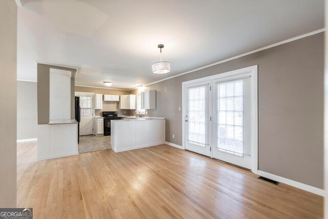 kitchen with black electric range oven, white cabinets, sink, hanging light fixtures, and light hardwood / wood-style flooring