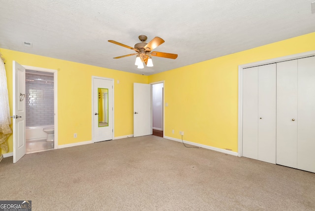 unfurnished bedroom with light carpet, a textured ceiling, ceiling fan, connected bathroom, and a closet