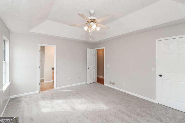 unfurnished bedroom with a tray ceiling, light carpet, ceiling fan, and a textured ceiling