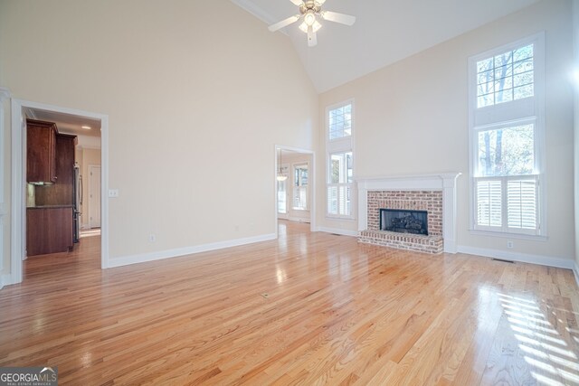 unfurnished living room with a high ceiling, light wood-type flooring, ceiling fan, and a healthy amount of sunlight