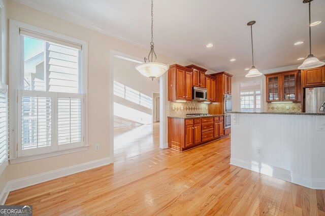 kitchen with a wealth of natural light, ornamental molding, stainless steel appliances, and light wood-type flooring