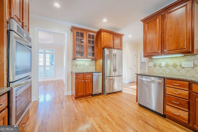 kitchen with appliances with stainless steel finishes, light hardwood / wood-style floors, light stone counters, and crown molding