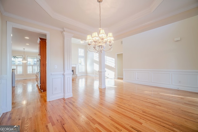 unfurnished dining area featuring decorative columns, a raised ceiling, a healthy amount of sunlight, and light wood-type flooring