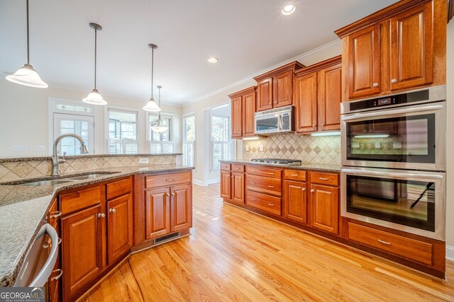 kitchen with tasteful backsplash, stainless steel appliances, sink, light hardwood / wood-style floors, and hanging light fixtures