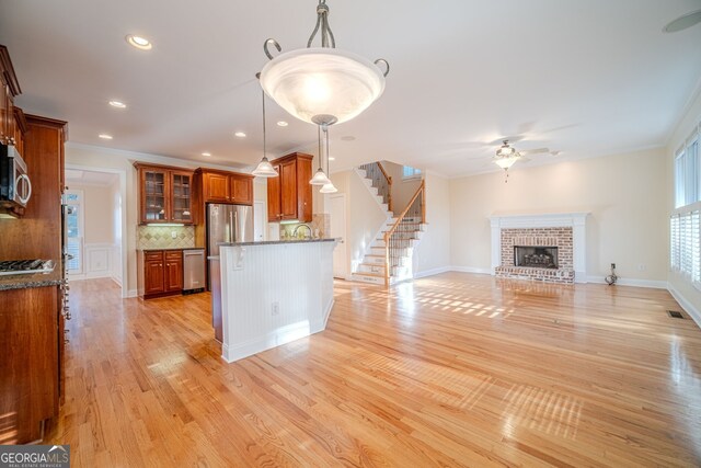 kitchen with light stone countertops, light wood-type flooring, crown molding, pendant lighting, and a fireplace