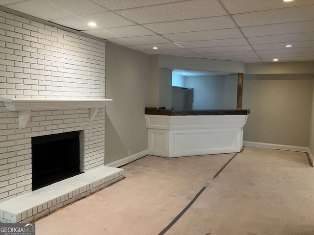 unfurnished living room featuring a drop ceiling, brick wall, and a brick fireplace