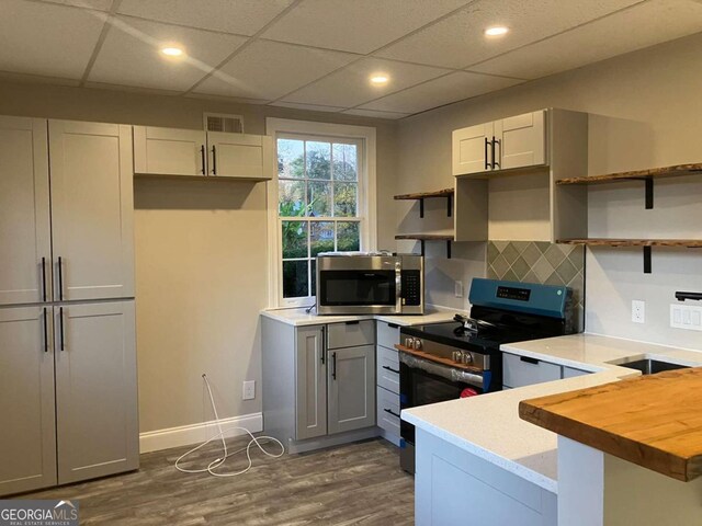 kitchen featuring gray cabinetry, a drop ceiling, stainless steel appliances, dark hardwood / wood-style floors, and butcher block countertops