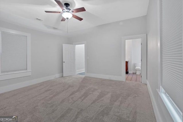 unfurnished bedroom featuring ceiling fan, light colored carpet, and ensuite bath