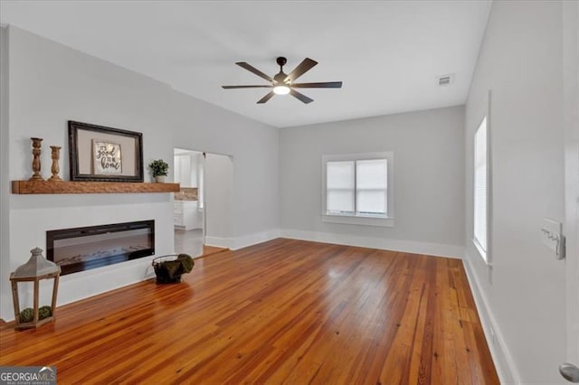 living room featuring visible vents, baseboards, a ceiling fan, a glass covered fireplace, and hardwood / wood-style floors