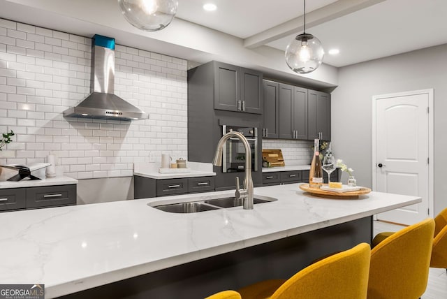 kitchen featuring gray cabinetry, backsplash, wall chimney exhaust hood, light stone countertops, and a breakfast bar area