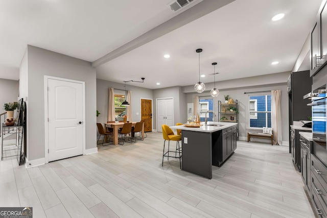 kitchen with light wood-type flooring, a breakfast bar, a kitchen island with sink, sink, and decorative light fixtures