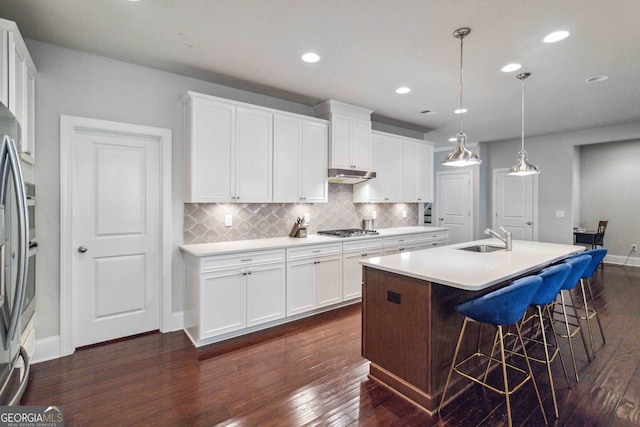 kitchen featuring stainless steel appliances, white cabinetry, dark wood-type flooring, and an island with sink