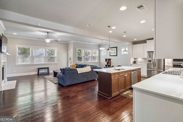 kitchen featuring appliances with stainless steel finishes, dark hardwood / wood-style flooring, ceiling fan with notable chandelier, white cabinetry, and an island with sink