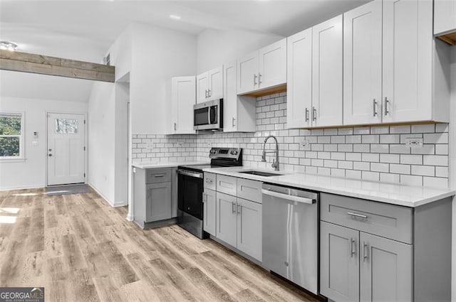 kitchen with backsplash, light hardwood / wood-style floors, stainless steel appliances, sink, and gray cabinets